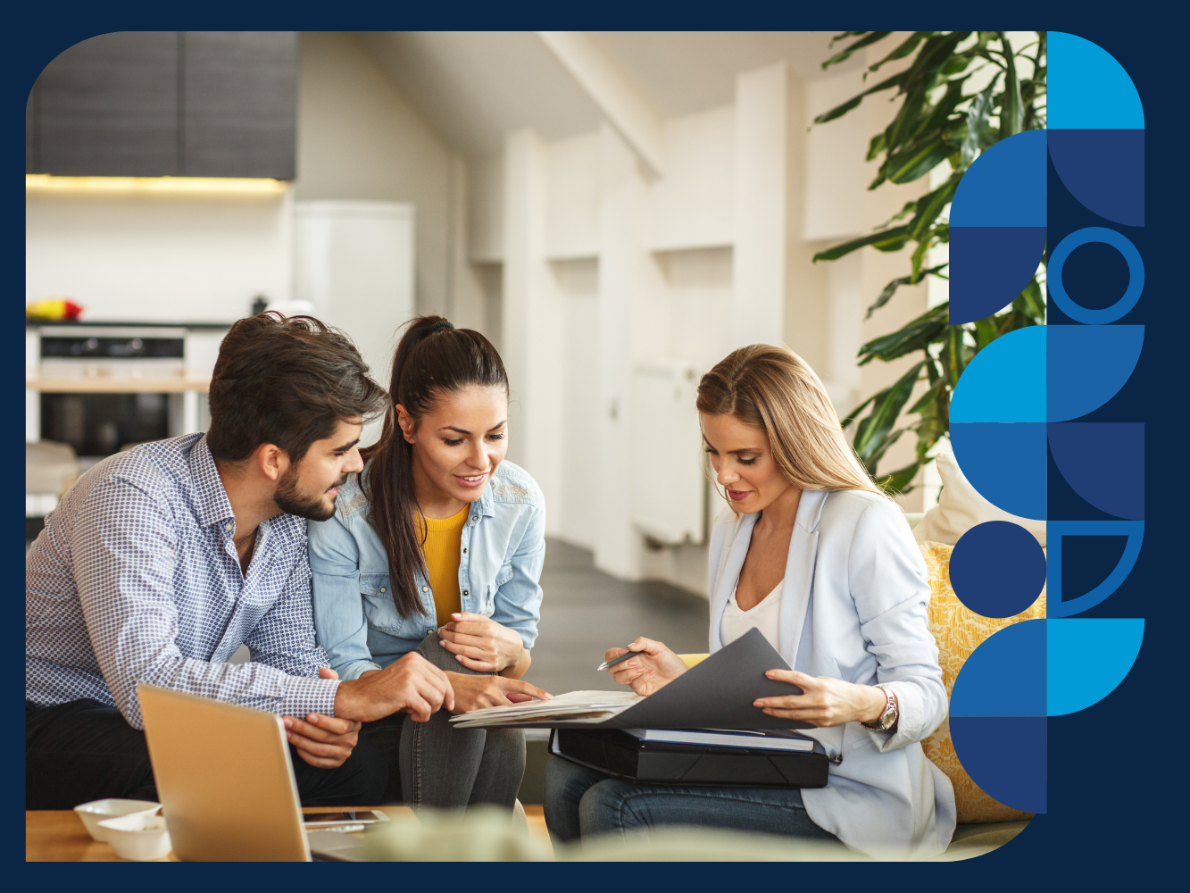 A group of three people having a discussion while looking at documents, with a laptop open on a table.